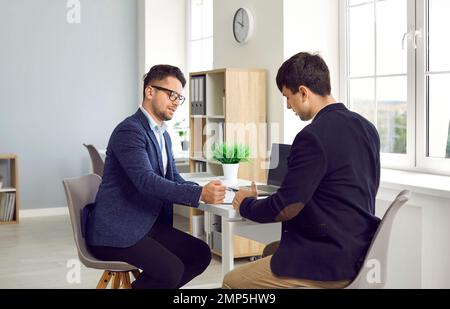 Homme d'affaires confiant discutant des termes du contrat avec le client masculin et montrant la place pour la signature Banque D'Images