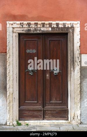 Vue sur l'ancienne porte en bois marron avec deux poignées de porte en métal de style oiseau dans un mur de couleur terre cuite à Venise, Italie. Bouton de porte Animatic Banque D'Images