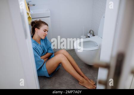 Jeune femme malade assise sur le sol près des toilettes. Banque D'Images