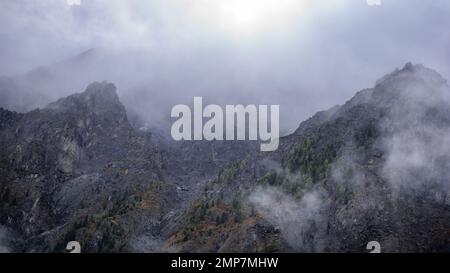 Le brouillard avec la neige et les nuages se déplace vers les montagnes en pierre avec des épinettes et des forêts sur des rochers abrupts après la pluie à Altai en été. Banque D'Images