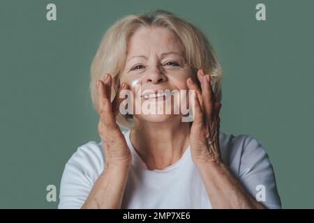 Belle femme âgée appliquant des cellules oculaires pour le bourrade tout en regardant l'appareil photo. Portrait de beauté. Soins de beauté. Soin du visage. Banque D'Images