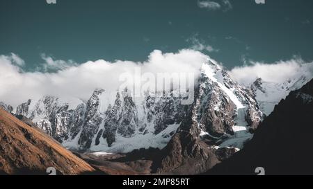 Les sommets des montagnes rocheuses avec des langues de glaciers et de neige sont couverts de nuages blancs et de brouillard en Altaï. Banque D'Images