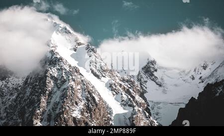 Les sommets des montagnes de pierre rocheuse avec des langues de glaciers et de neige sont couverts de nuages blancs et de brouillard en Altaï par une journée de forte luminosité. Banque D'Images