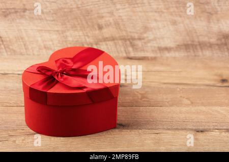 Boîte cadeau rouge en forme de coeur avec noeud rouge sur fond en bois avec espace pour le texte. Bonne Saint Valentin, fête des mères et anniversaire greetin Banque D'Images