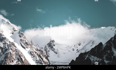 Panorama des sommets des montagnes rocheuses avec des langues de glaciers et de neige couvertes de nuages blancs et de brouillard en Altaï. Banque D'Images