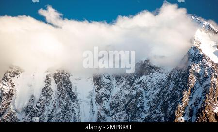 Panorama des sommets des montagnes de pierre rocheuse avec des langues de glaciers et de neige couvertes de nuages blancs et de brouillard en Altaï par une journée de forte luminosité. Banque D'Images