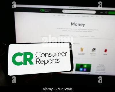 Personne tenant un smartphone avec le logo de l'organisation américaine Consumer Reports (CR) à l'écran devant le site Web. Mise au point sur l'affichage du téléphone. Banque D'Images