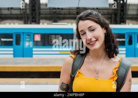 belle jeune femme latine d'origine argentine, vêtue de jaune, est assise sur la plate-forme, regardant la caméra et souriant heureux parce que s. Banque D'Images