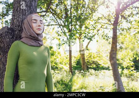 Jeune fille musulmane embrassant un arbre. Gros plan d'une jeune femme dans un hijab et de vêtements décontractés dans le parc. Protéger l'environnement et les soins Banque D'Images