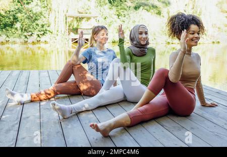 Groupe d'adolescents est engagé dans la forme physique sur la jetée au bord du lac ou de la rivière. Les jeunes filles et les filles positives vont dans le sport. Musulman dans un hijab, afro-américain A. Banque D'Images