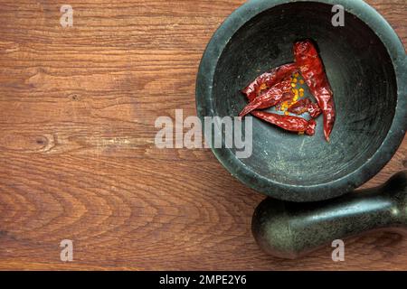 Piment rouge dans un mortier de granit en pierre, piments séchés croquants vue de dessus sur fond de bois copie espace Banque D'Images