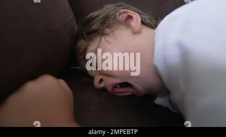 Un petit garçon dormant sur un canapé. Enfant fatigué gros plan bâillements de visage s'endormit Banque D'Images