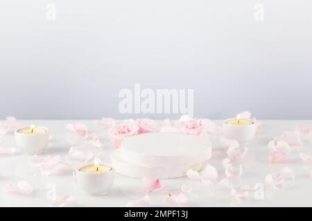 Podium vide en bois avec roses roses, pétales et bougies sur table blanche. Scène de concept vitrine pour nouveau produit, promotion vente, présentation, co Banque D'Images