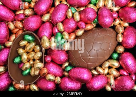 Pile ou groupe de plusieurs couleurs et différentes tailles d'oeufs de pâques au chocolat enveloppés d'une feuille colorée dans le rose, le rouge, l'or et le vert lime avec deux moitiés o Banque D'Images