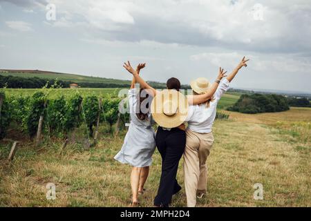 Trois jeunes femmes s'embrasent et marchent sur le vignoble. Les amies blanches vêques et chapeaux ont du plaisir sur le terrain. Bonnes filles ar Banque D'Images