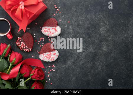 Biscuits au velours rouge ou au brownie sur le coeur en forme de glaçage au chocolat avec roses rouges et boîte cadeau sur fond noir. Idée de dessert pour la Saint-Valentin, Mot Banque D'Images