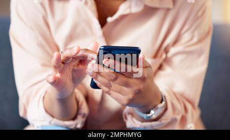 Gros plan des mains textant sur le téléphone, tapant des messages sur les médias sociaux et effectuant des recherches ou défilant en ligne. Femme décontractée assise seule sur le canapé de la salle de séjour Banque D'Images