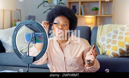 Afro beauté influenceur, enregistreur ou animateur de podcast parlant, en utilisant le téléphone pour filmer en direct flux de maquillage tutorial avec nouveau maquillage mascara. Femme excitée utilisant Banque D'Images