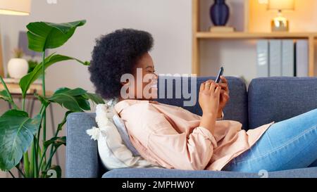 Une jeune femme qui rit envoie un SMS sur un téléphone à la maison. Une femme joyeuse bavarde avec ses amis sur les réseaux sociaux, navigue en ligne et regarde drôle Banque D'Images
