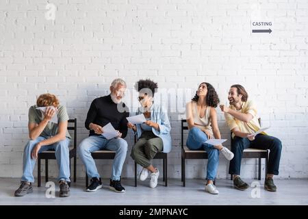 femme afro-américaine montrant un scénario à un acteur barbu près de demandeurs d'emploi en attente de casting Banque D'Images