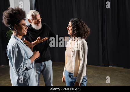 souriant directeur d'art pointant avec la main et parlant à une femme multiraciale près de l'actrice afro-américaine dans le théâtre Banque D'Images