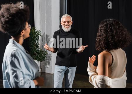 joyeux homme aux cheveux gris pointant avec le pouce près des actrices multiethniques dans l'école de compétences d'action Banque D'Images