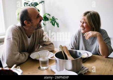 Heureux couple d'âge mûr parlant l'un à l'autre assis à table de salle à manger dans la maison Banque D'Images