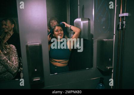 Une jeune femme heureuse qui apprécie ses amis tout en regardant le miroir dans la salle de bain de la discothèque Banque D'Images