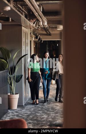 Souriantes femmes d'affaires multiraciales discutant pendant qu'elles marchent au bureau Banque D'Images