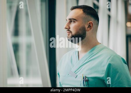 Infirmière masculine réfléchie regardant par la fenêtre dans l'hôpital Banque D'Images