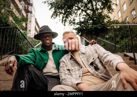 Portrait d'amis masculins multiraciaux assis les uns avec les autres sur les marches Banque D'Images
