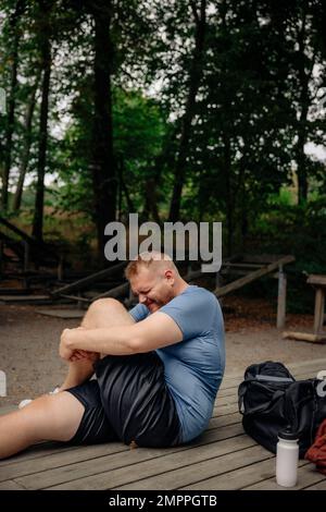 Vue latérale d'un homme obèse qui s'étire les jambes tout en étant assis sur un banc au parc Banque D'Images