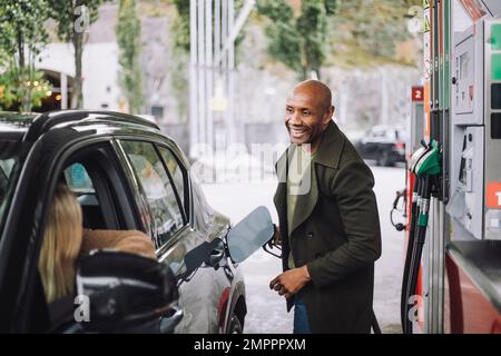 Homme à la tête rasée parlant à une femme en ravitaillant en carburant à la station-service Banque D'Images