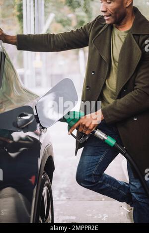 Homme mature pompant du gaz dans la voiture en se tenant à la station-service Banque D'Images