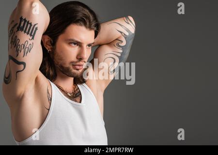 Homme moulant tatoué dans le haut blanc de réservoir posant isolé sur le gris Banque D'Images