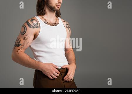 Vue rognée de l'élégant homme tatoué posant dans le débardeur isolé sur gris Banque D'Images