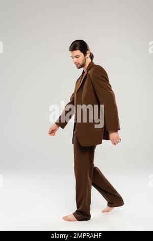 Homme long et élégant en costume marchant sur fond gris Banque D'Images