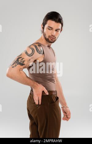 Brunette barbu homme avec tatouage posant isolé sur gris Banque D'Images
