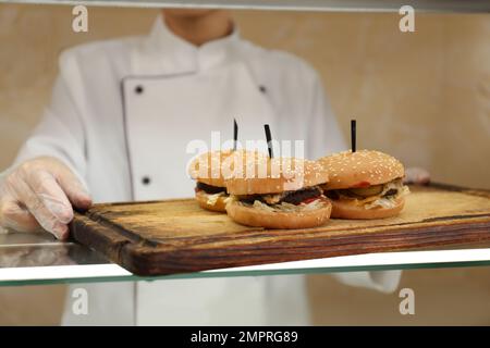 Employé de cantine d'école avec hamburgers à la ligne de service, clôture. Nourriture savoureuse Banque D'Images