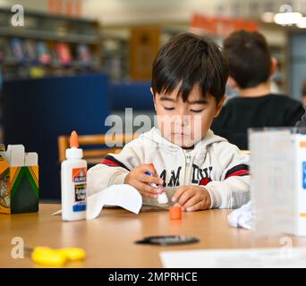 Un jeune garçon utilise un bâton de colle pour faire un totem pendant le temps de stockage de la bibliothèque de Bateman's avec les enfants à la base conjointe Langley-Eustis, Virginie, le 16 novembre 2022. La hauteur moyenne d'un totem est de 70 pieds et doit être vue n'importe où dans un village. Le totem le plus haut au monde est de 173 pieds et appartient à la tribu Kwakwwaka’wakw. Banque D'Images