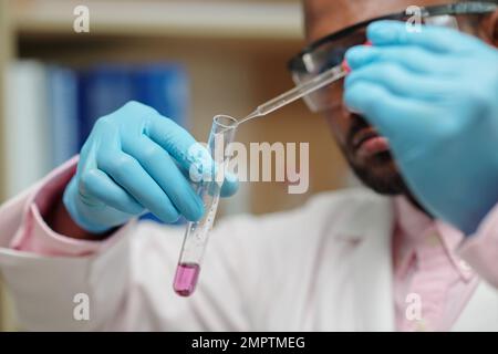 Chercheur utilisant une pipette lors de la dépose du réactif dans un tube à essai avec du liquide rose Banque D'Images