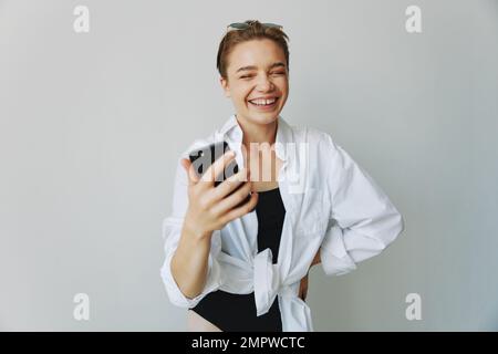 Une jeune fille blogger prend des photos et des pousses. elle-même sur la vidéo sur son téléphone pour le contenu de médias sociaux, blogueur vidéo, se selfie contre un mur blanc avec Banque D'Images