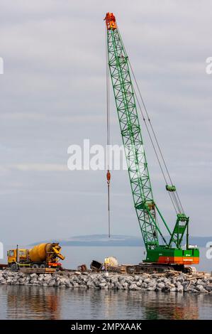 Chantier de construction portuaire Irlande - travaux de génie civil humide en cours sur le pont-jetée en pierre avec mélangeur de ciment et grue verte sur l'île d'Inishmore. Banque D'Images