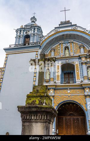 La façade colorée et le clocher peint de l'église Saint-Domingue de Guzman à Ocotlan de Morelos, Oaxaca, Mexique, avec une croix en pierre devant Banque D'Images