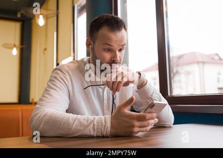 Un homme d'affaires élégant et surpris, un homme d'affaires d'Europe, tient des lunettes dans sa main et regarde dans son smartphone. Banque D'Images