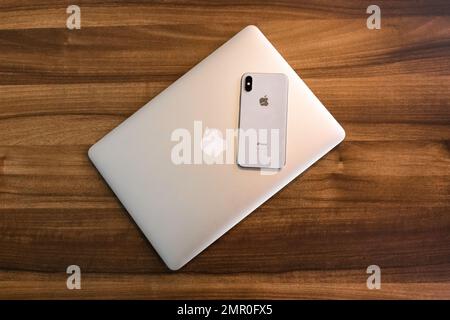 Biélorussie, région de Minsk - 17 mars 2020: Apple smartphone iPhone et ordinateur portable se trouvent sur un bureau en bois de bureau lieu de travail s'est opposé à des gadgets modernes. Banque D'Images