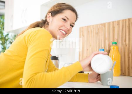 femme versant du lait dans son café Banque D'Images