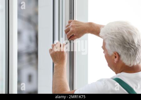 Ouvrier de construction mûr réparant les fenêtres en plastique à l'intérieur Banque D'Images