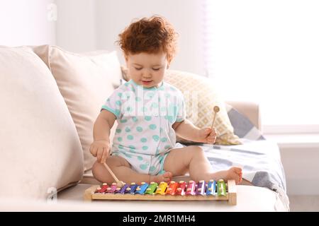 Mignon petit enfant jouant avec xylophone sur le canapé à la maison Banque D'Images