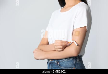 Jeune femme avec timbre de nicotine et cigarette sur fond gris clair, gros plan Banque D'Images